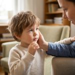 Une mère réconforte son jeune fils touché à la bouche dans un salon lumineux.